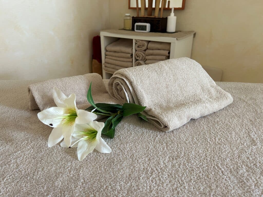 Beigefarbene Handtücher und weiße Lilie auf dem aufgeräumten Massagetisch.