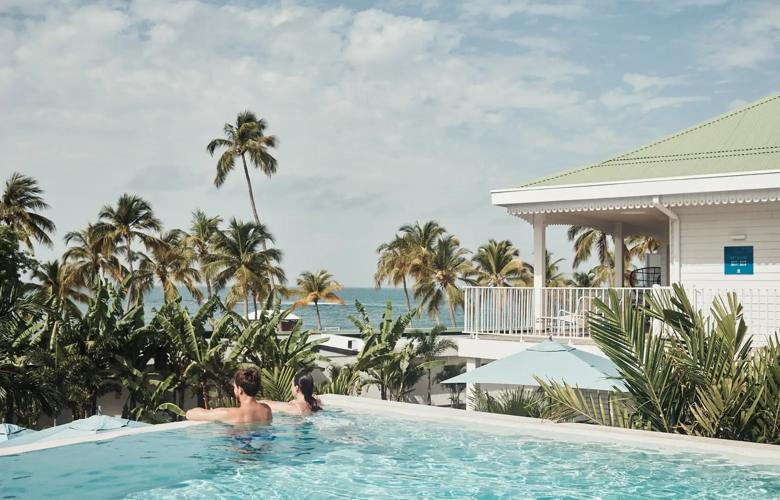 Zwei Personen entspannen sich in einem tropischen Pool mit Meerblick.