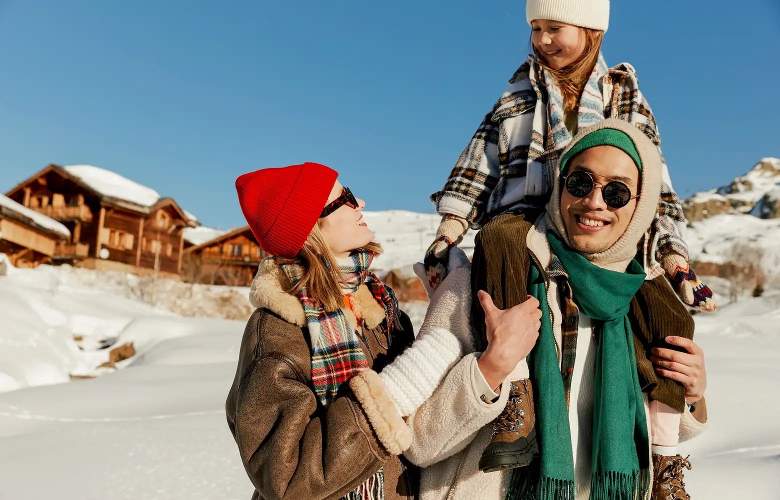 Drei Personen in Winterkleidung stehen draußen inmitten verschneiter Gebäude.