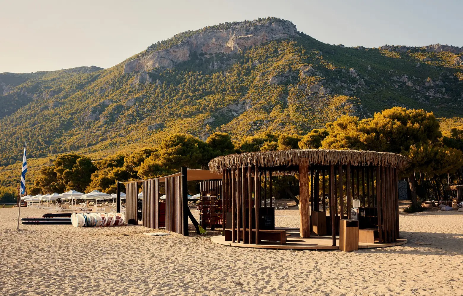 Strohgedeckte Holzhütte am Strand, dahinter Berge und Bäume.