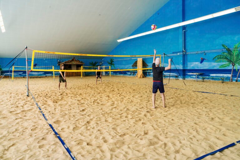 Drei spielen drinnen Beachvolleyball, Wandmalerei aus Palmen und helle Lichter.