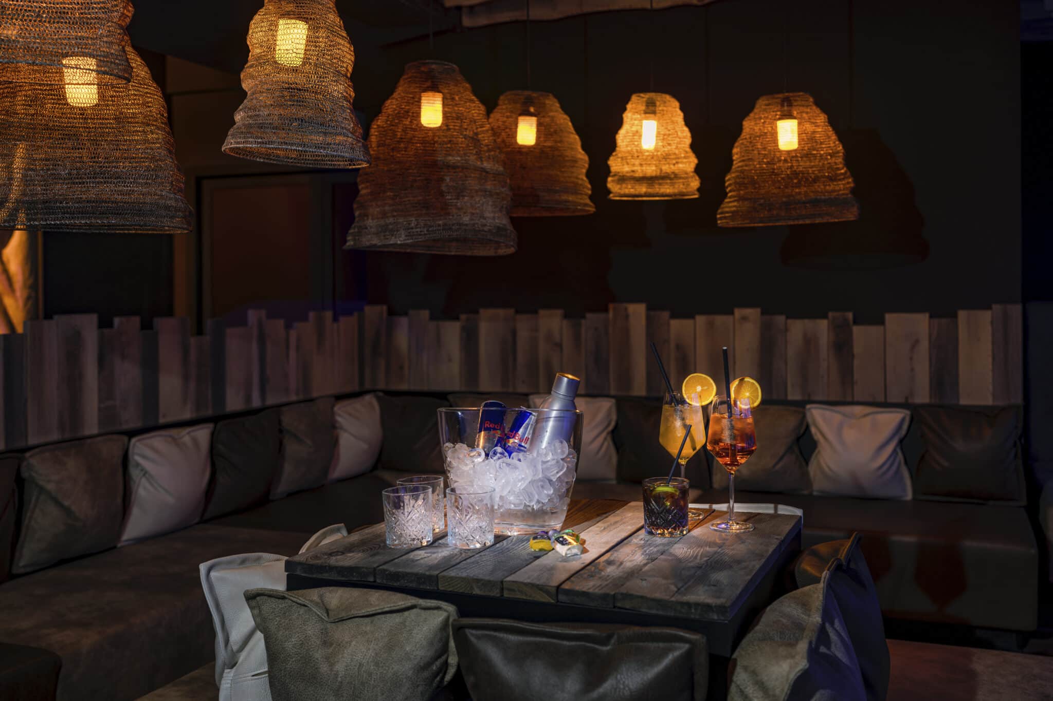 Gemütlicher Aufenthaltsraum: Holztisch, Getränke auf Eis, sanfte Beleuchtung, Kissen.