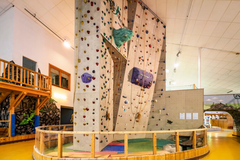 Indoor-Kletterwand mit bunten Griffen, Seilen, gepolstertem Boden und Balkon.