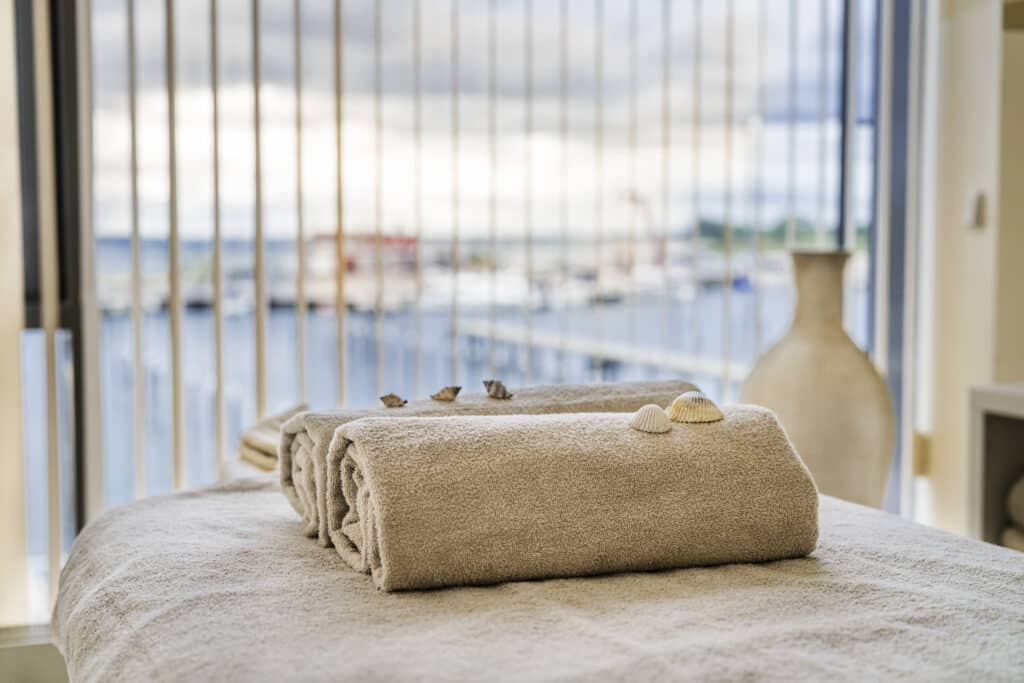 Beige Handtücher mit Muscheln auf dem Spa-Tisch, Blick auf den Yachthafen.