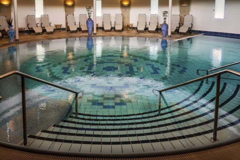Innenpool mit Stufen, Liegestühlen, Statuen und Sonnenlicht.