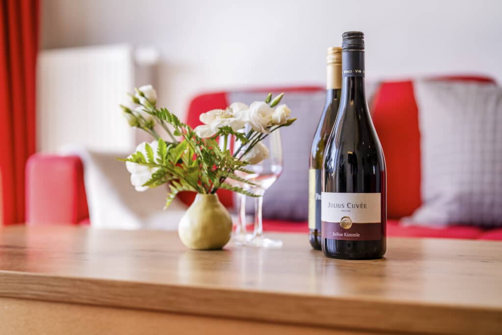Wein, Glas und Blumen auf dem Tisch vor der roten Couch.