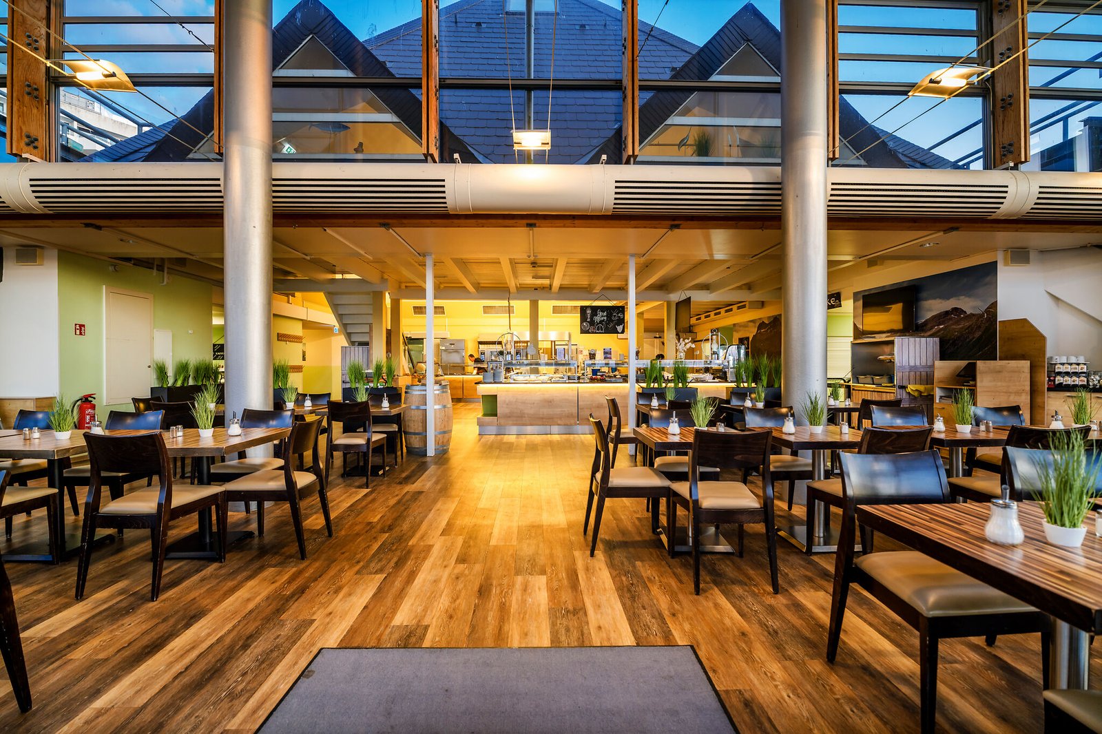 Modernes, geräumiges Restaurant mit Holzböden, Pflanzen, offener Küche.