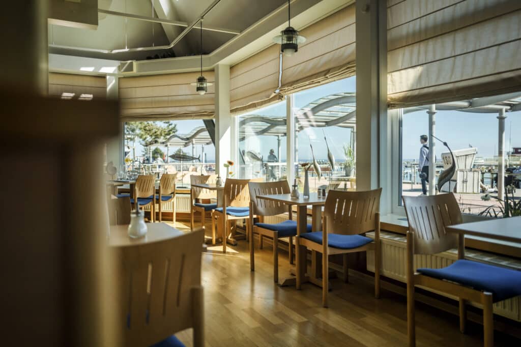 Helles, modernes Restaurant, Holztische, blaue Kissen, Blick aufs Meer.