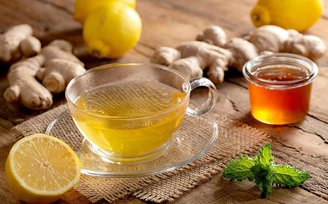 Gläserne Tasse Tee mit Zitrone, Ingwer, Honig und Minze.