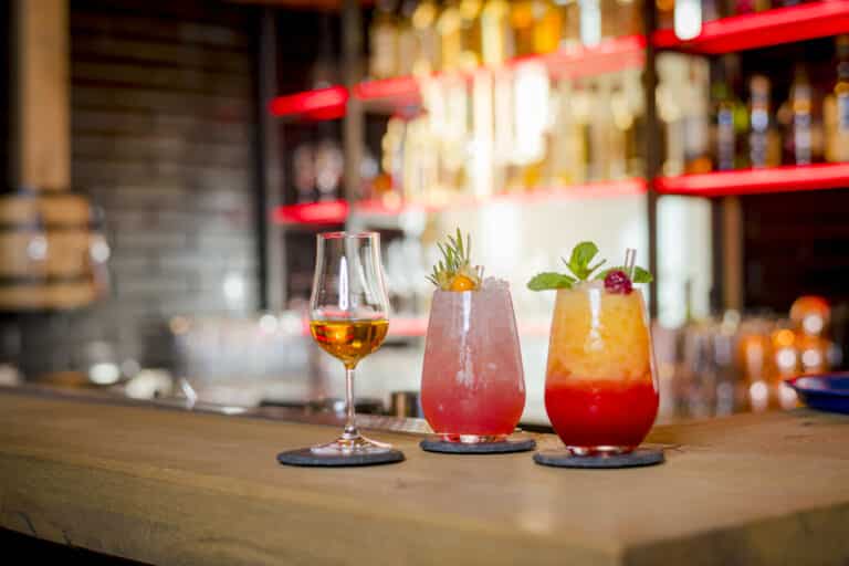 Bernsteinfarbener Schnaps und bunte Cocktails auf Untersetzern an der lebhaften Bar.