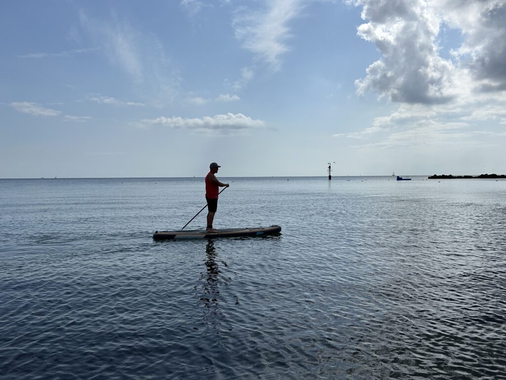 Hat_red_shirt_SUP_Verleih: Paddleboarder auf ruhigem Meer in der Nähe des Strandverleihs.