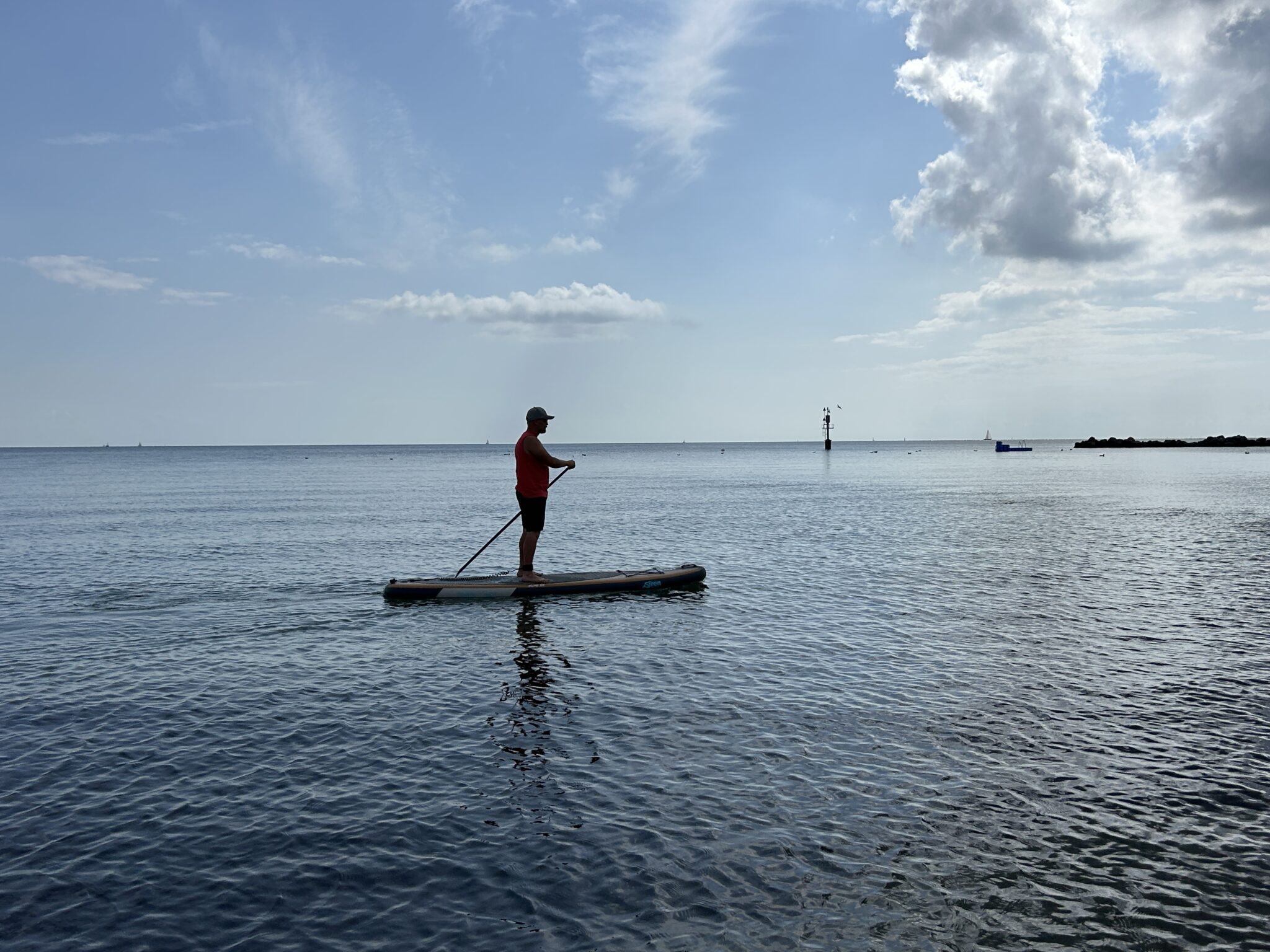 Hat_red_shirt_SUP_Verleih: Paddleboarder auf ruhigem Meer in der Nähe des Strandverleihs.