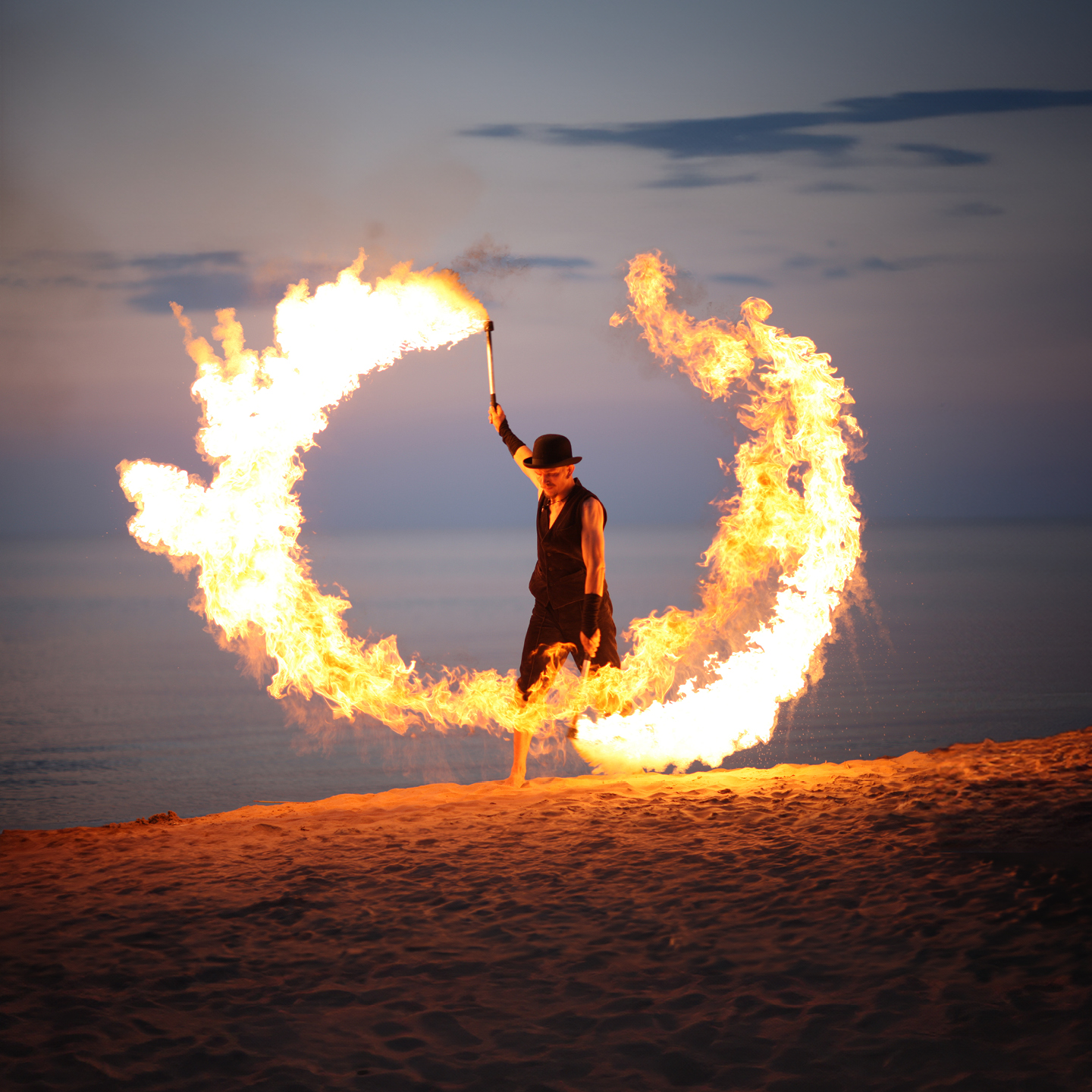 Fire_dancer_beach.jpg: Performerin kreiert feurigen Ring am Strand in der Abenddämmerung.