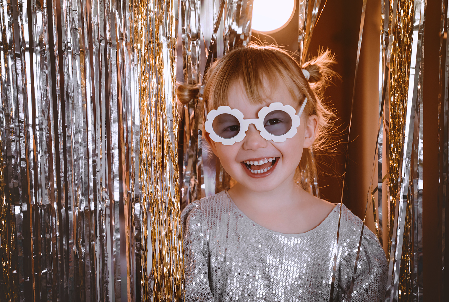 Silvester_familienhotel_child.jpg: Lächelndes Kind mit Brille, Paillettenoberteil, Lametta-Kulisse.