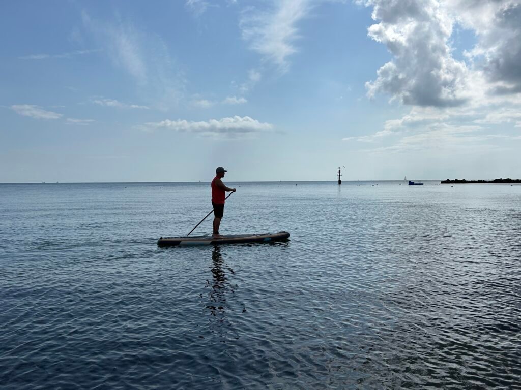Hat_red_shirt_SUP_Verleih: Paddleboarder auf ruhigem Meer in der Nähe des Strandverleihs.
