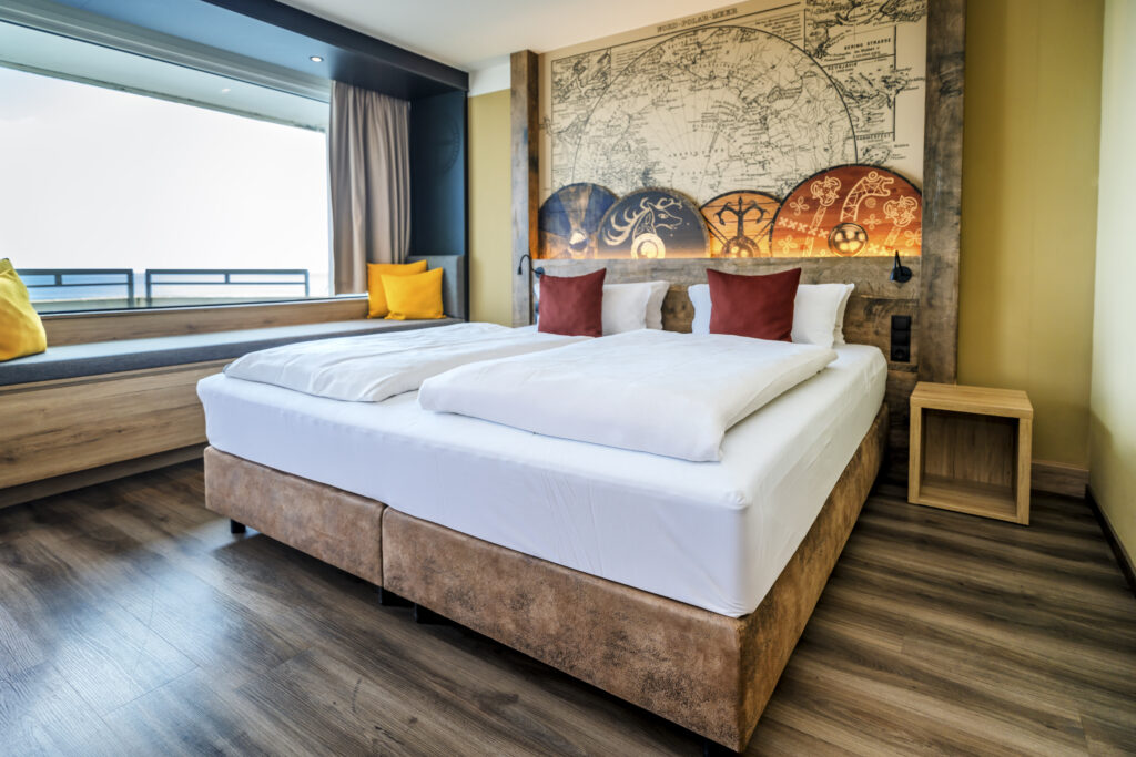 Hotelzimmer_birgitfoerster: Doppelbett, Wandbild mit Landkarte, rote Kissen, gelbe Fensterbank.