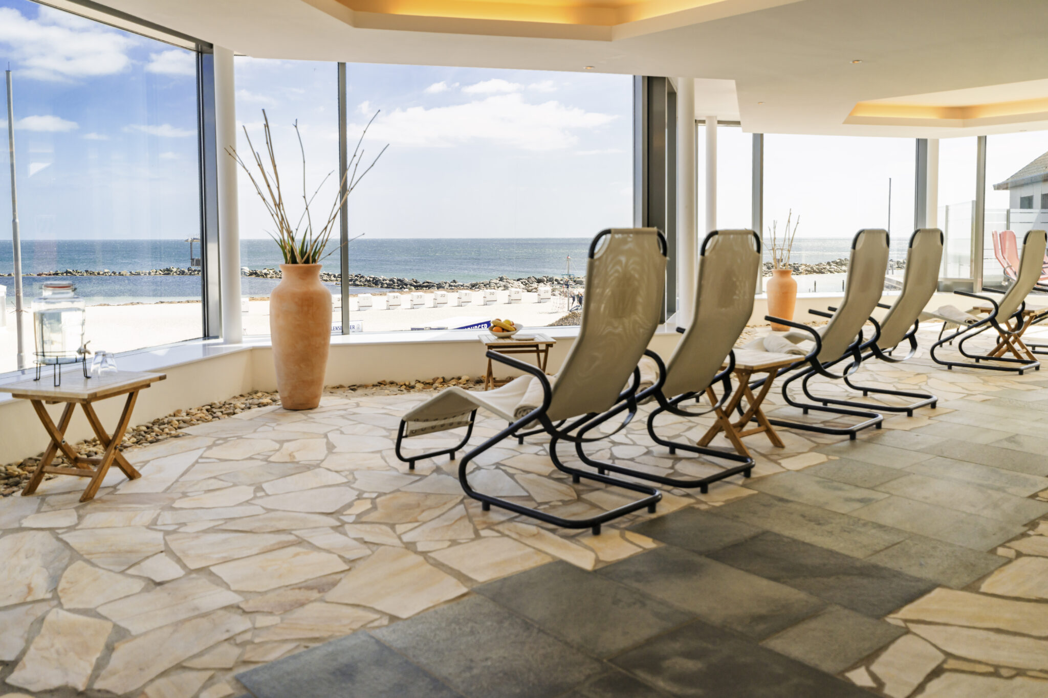 Beach_lounge_view.jpg: Leere Liegestühle, Blick auf das Meer, heller, sonnenbeschienener Raum.