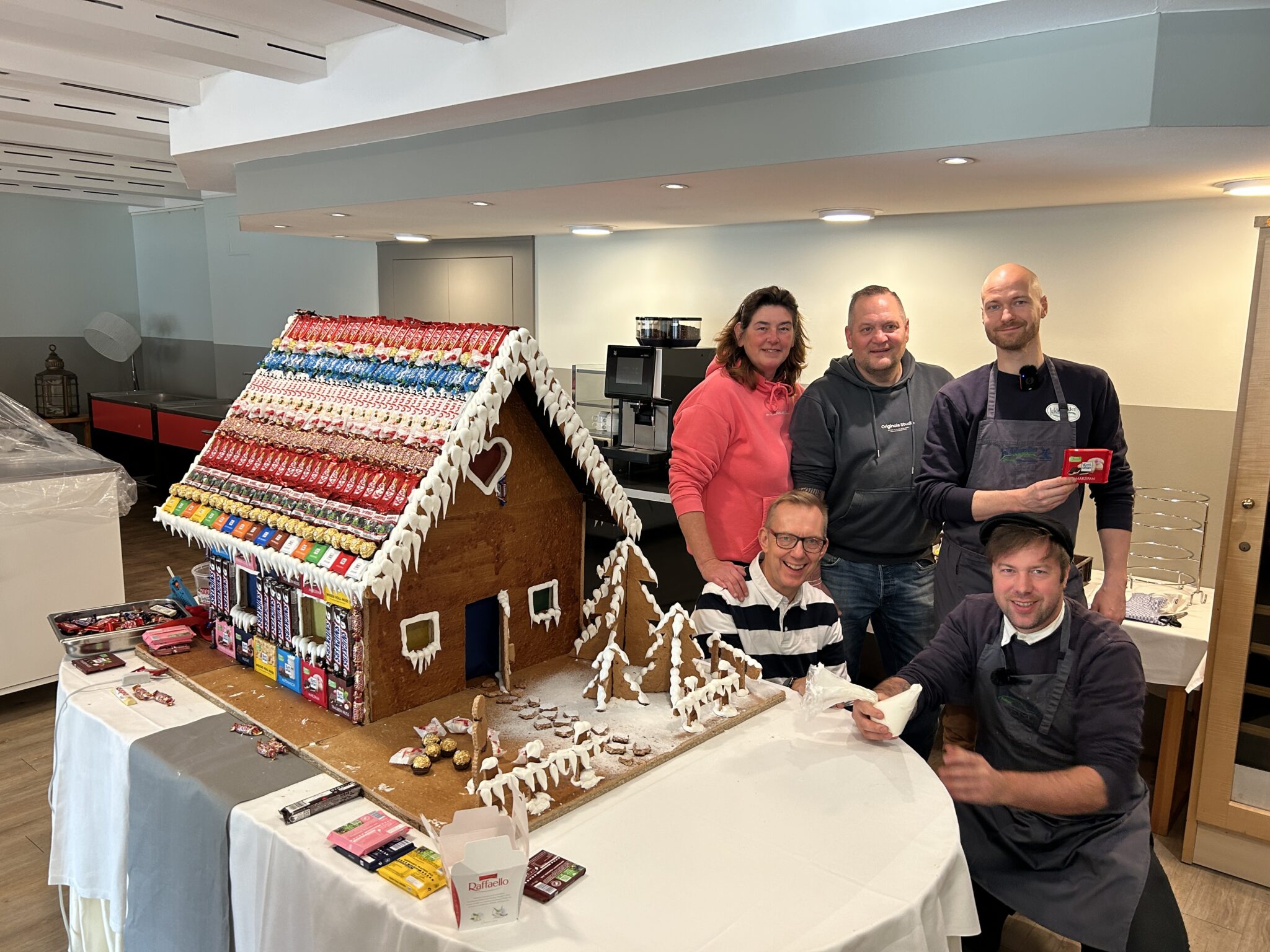 Spitzbergen_kuchenbuffet: Fünf Erwachsene mit aufwändigem Lebkuchenhaus, drinnen.