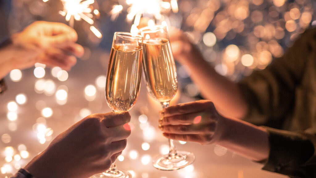 Drei Hände stoßen mit Champagner inmitten funkelnder Lichter an.
