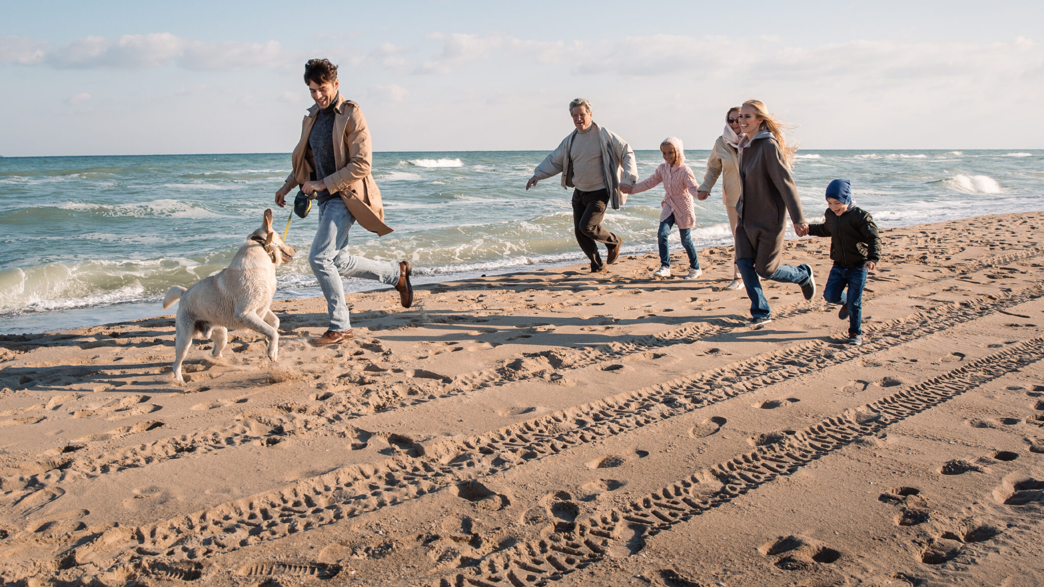 Beach_run001: Erwachsene, Kinder und Hund laufen am Sandstrand, Jacken an.