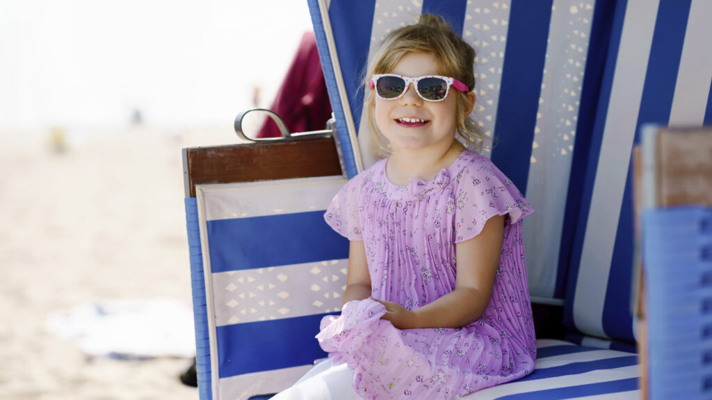 Beachgirl_summer.jpg: Junges Mädchen im rosa Kleid lächelt auf einem Strandkorb.