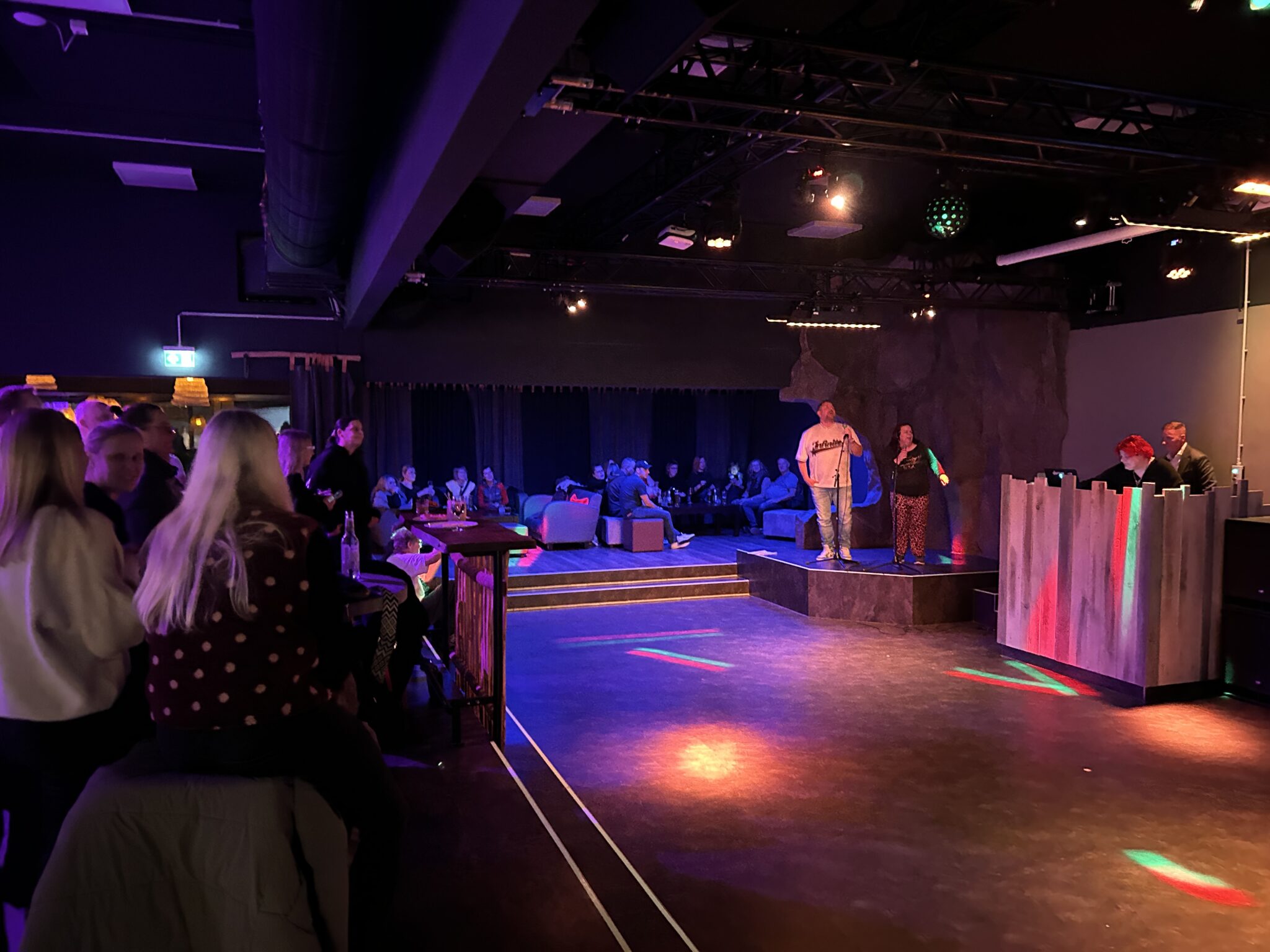 Kubbsala-karaoke-night: schummriger Veranstaltungsort, lebhaftes Publikum, farbige Bodenbeleuchtung.