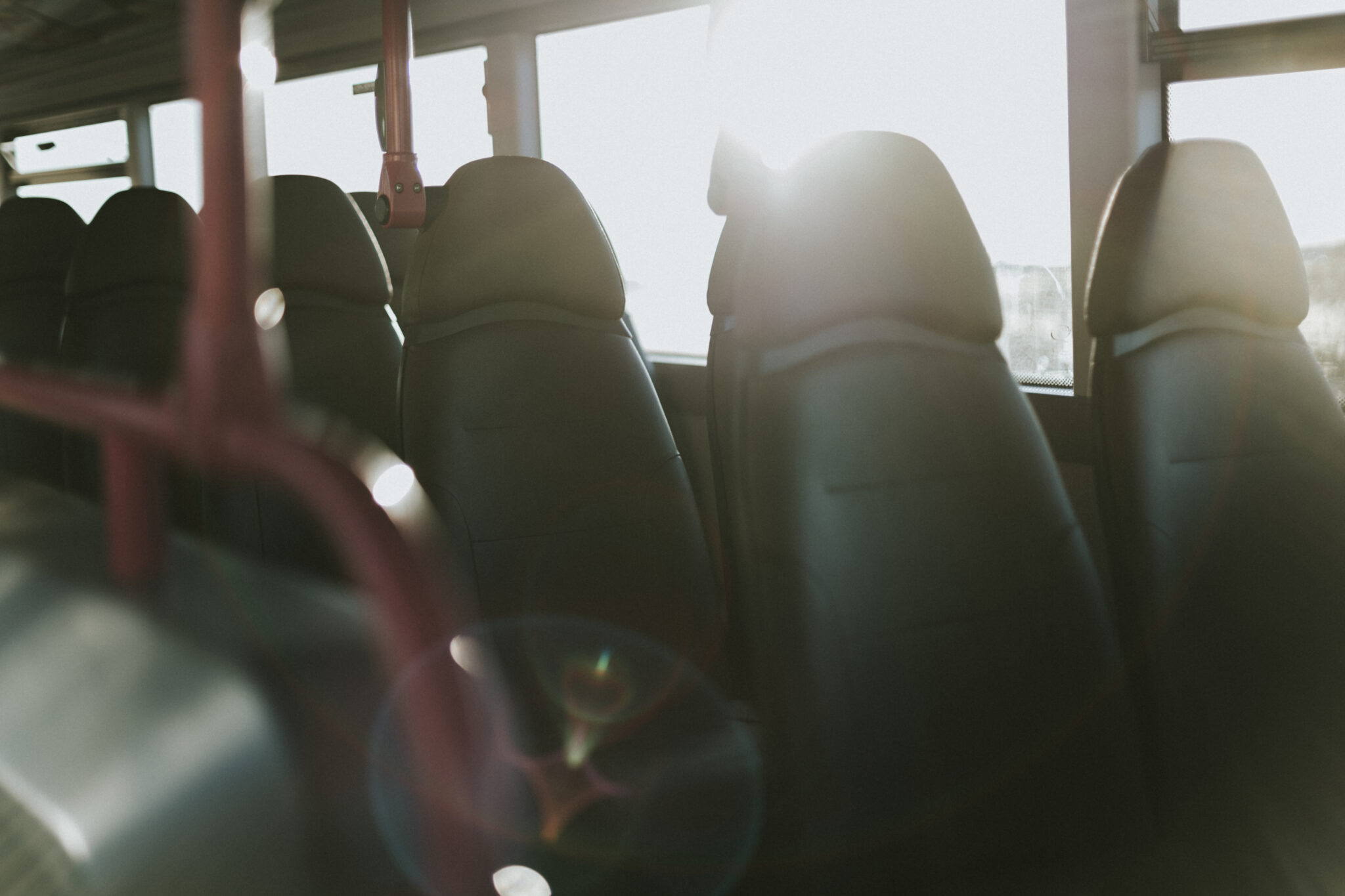 Bus-seats.jpg: Schwarze Sitze im Sonnenlicht, rote Stangen, Streulicht im Bus.