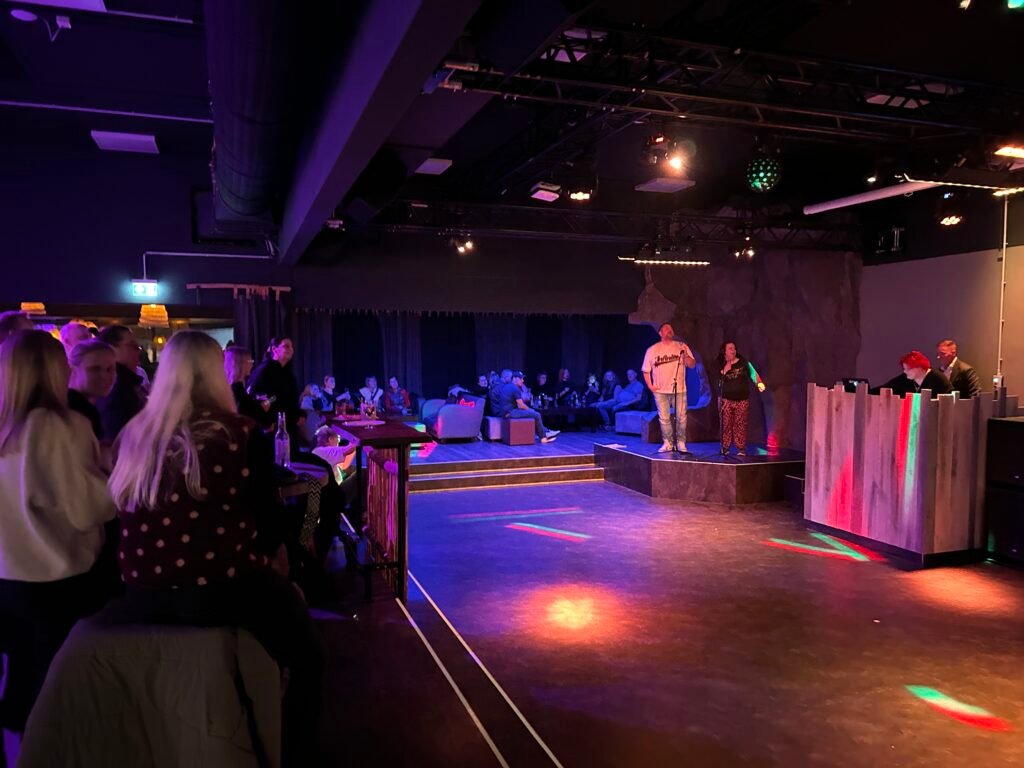 Kubbsala-karaoke-night: schummriger Veranstaltungsort, lebhaftes Publikum, farbige Bodenbeleuchtung.
