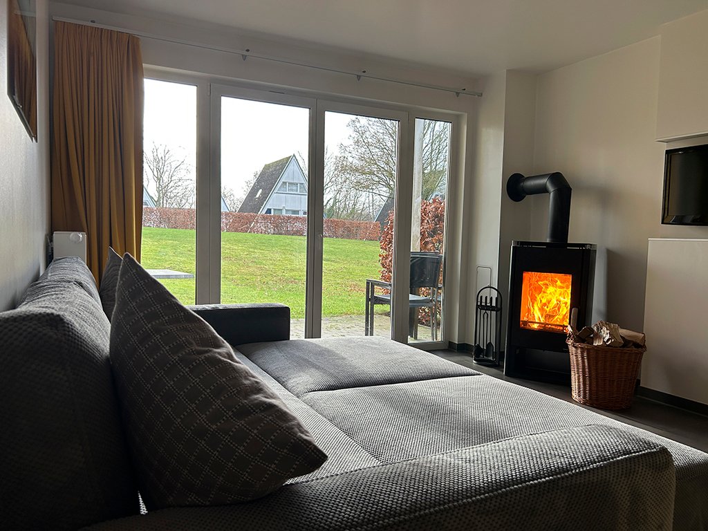 Gray seating area, wood-burning stove, glass doors, view outside.