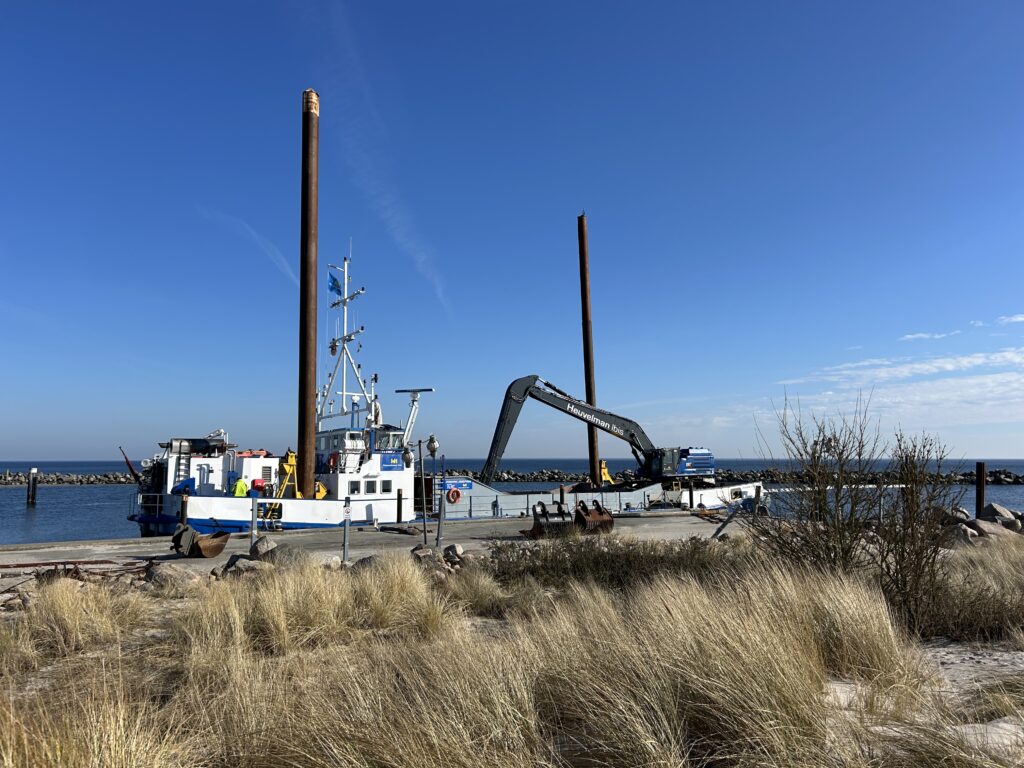 Feuchte_Hafen_Ansicht: Dock, blau-weißes Boot, Kran, Rostpfähle, Gras.