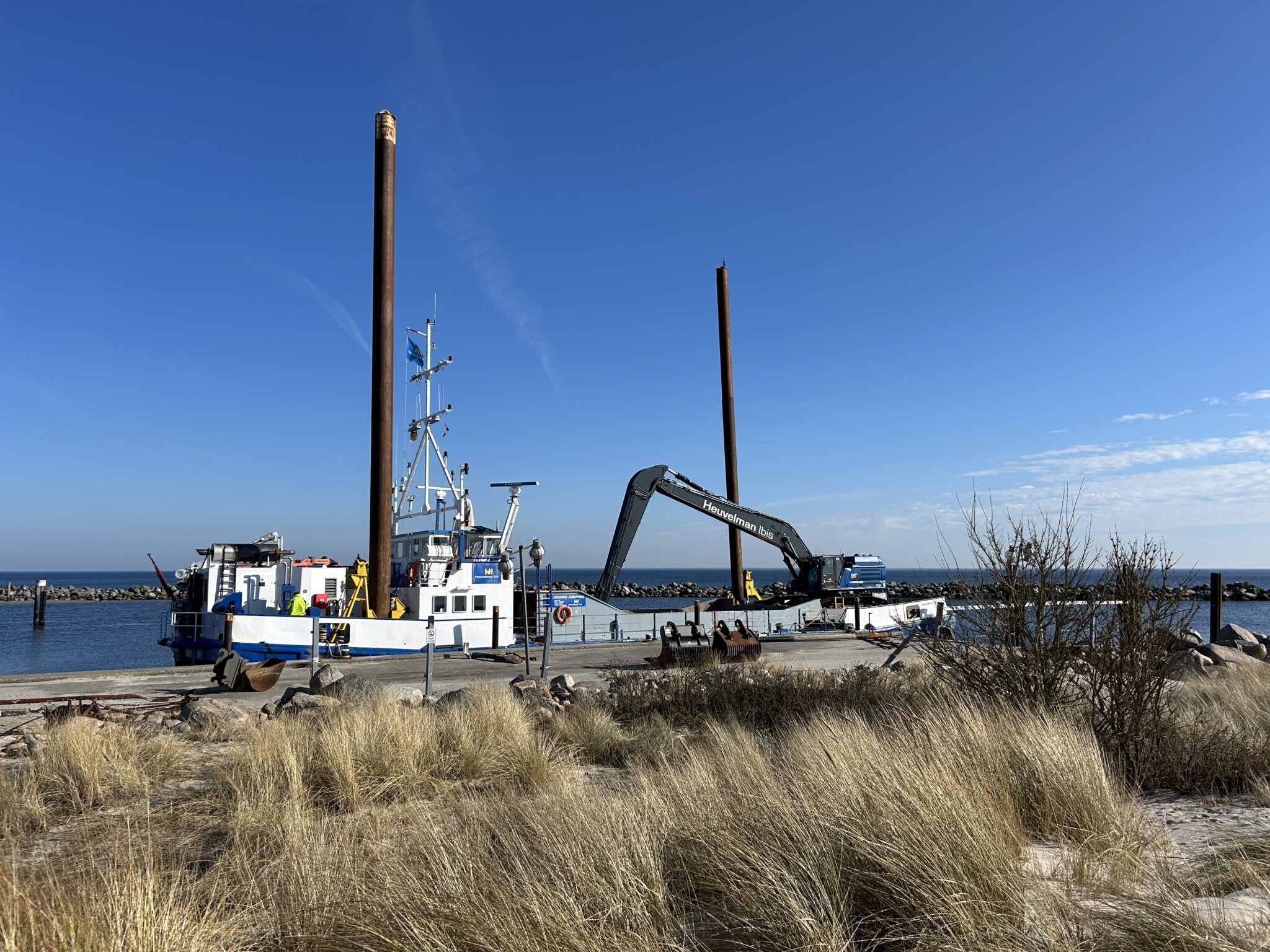 Feuchte_Hafen_Ansicht: Dock, blau-weißes Boot, Kran, Rostpfähle, Gras.