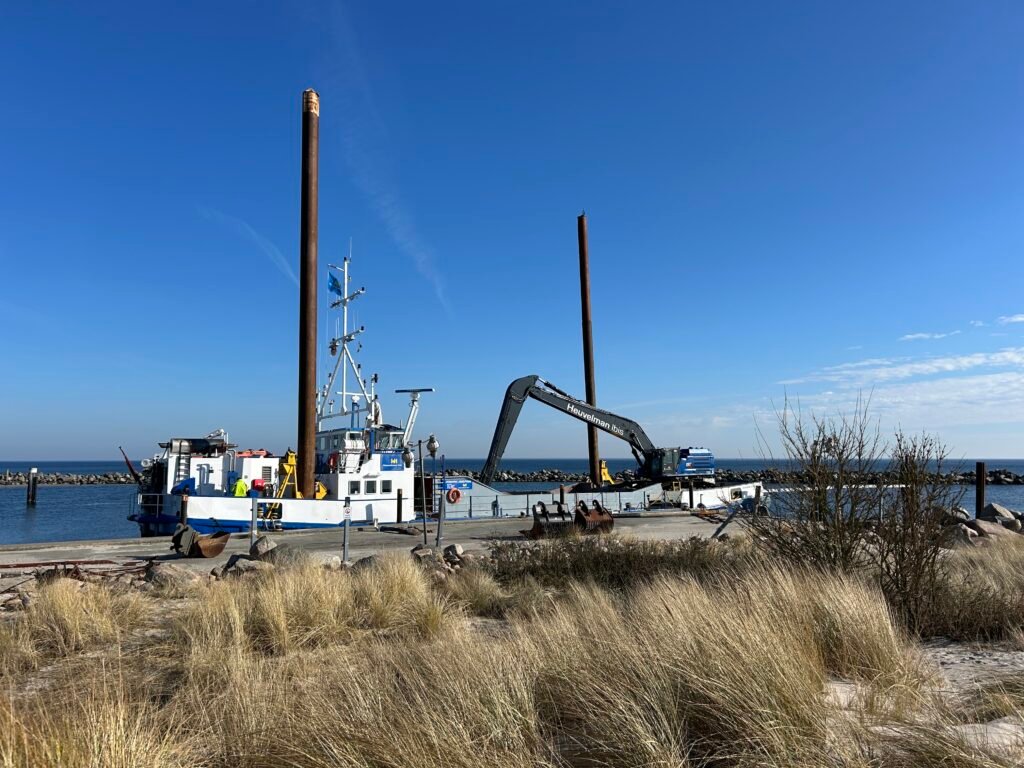 Feuchte_Hafen_Ansicht: Dock, blau-weißes Boot, Kran, Rostpfähle, Gras.