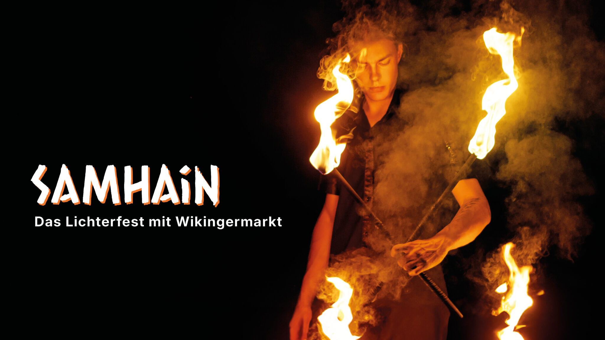 Samhain an der Ostsee. Person wirbelt mit Feuerstäben, "SAMHAIN"-Schriftzug leuchtet links.
