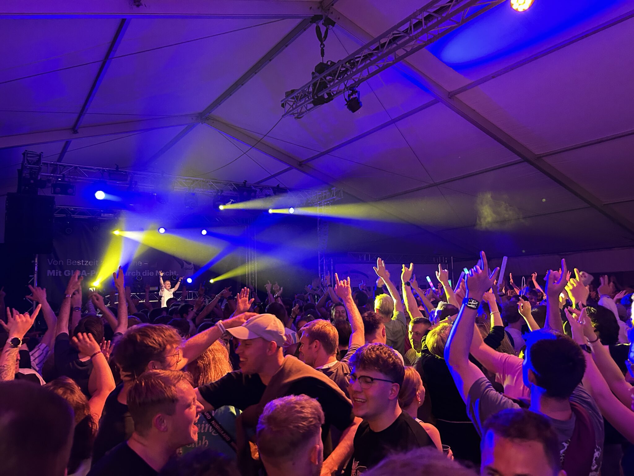 Concert_crowd_tent.jpg: Die Menge jubelt unter dem Zelt mit Scheinwerfern, WM-Energie.