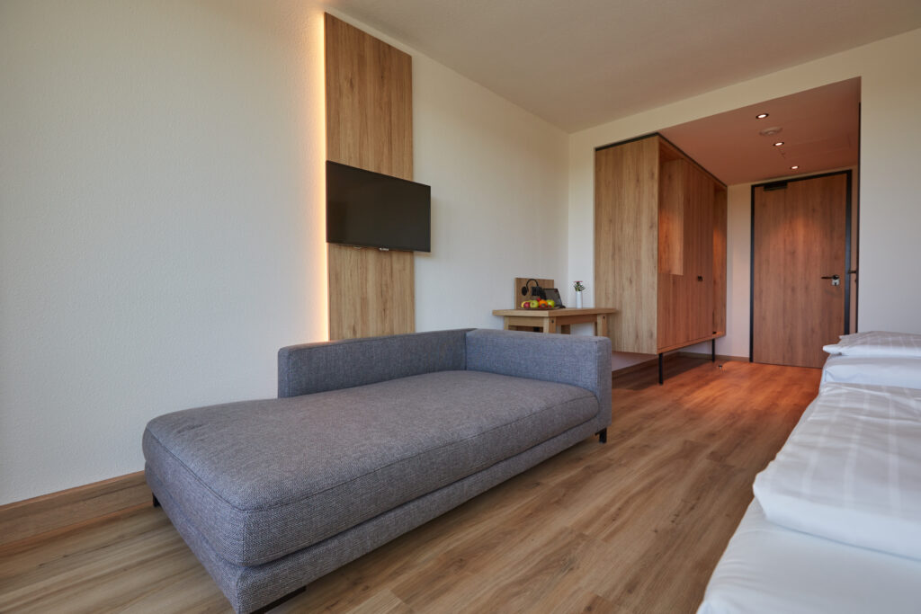 Midgard_room.jpg: Minimalistisches Ostseehotel-Zimmer mit Sofa, Schreibtisch, Bett, TV.