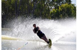 File_water-skiing.jpg: Wasserskifahrer in der Nähe des Freizeithotels; Kinder, Bäume und Grünflächen sind zu sehen.