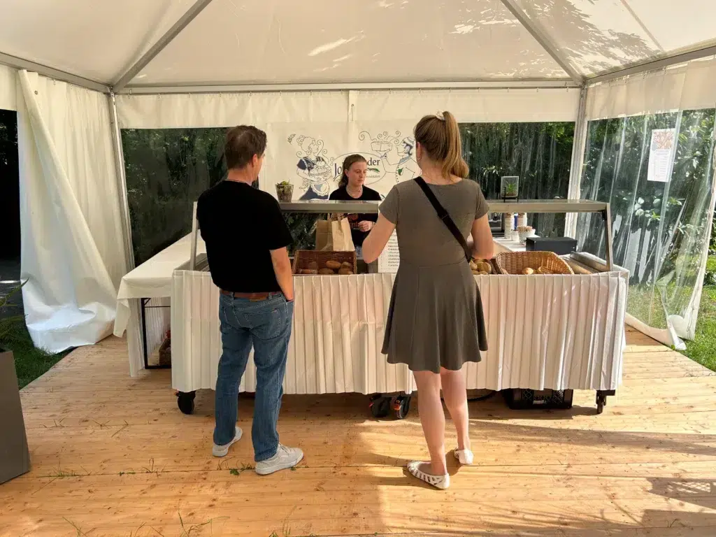 Ostsee_damp_bakery.jpg: Zwei Personen kaufen Brot an einem Brötchenverkaufsstand im Freien.