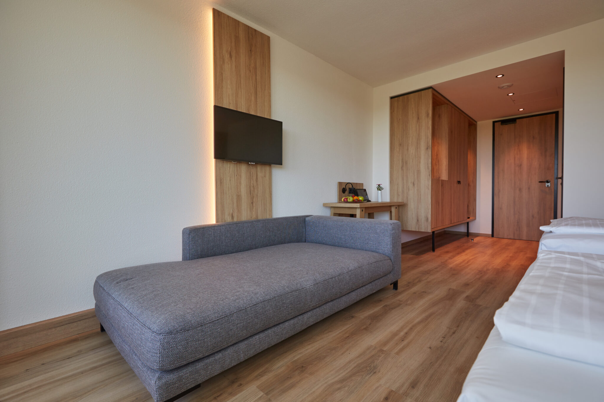 Hotelroom_interior.jpg: Modernes Zimmer, Holzböden, graues Sofa, Schreibtisch, Bett (Teilansicht).