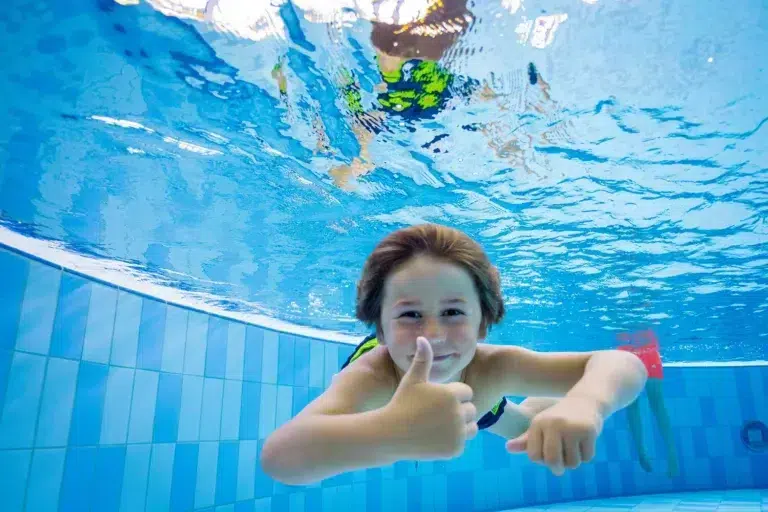 Ein Kind schwimmt unter Wasser und lächelt im Schwimmbad des Ostsee Resorts Damp.