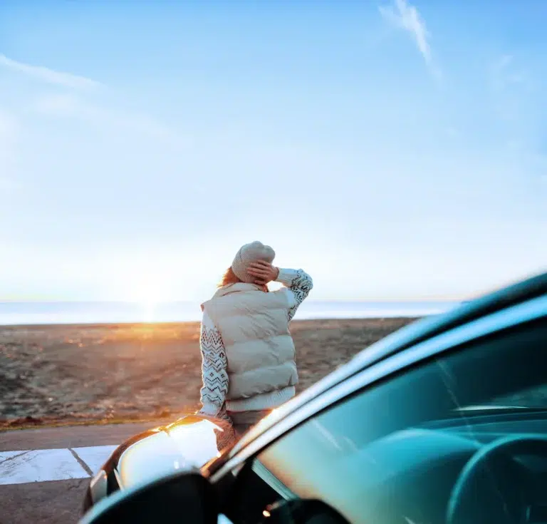 Eine Frau, die sich am Strand des Ostsee Resorts Damp an ein Auto lehnt.