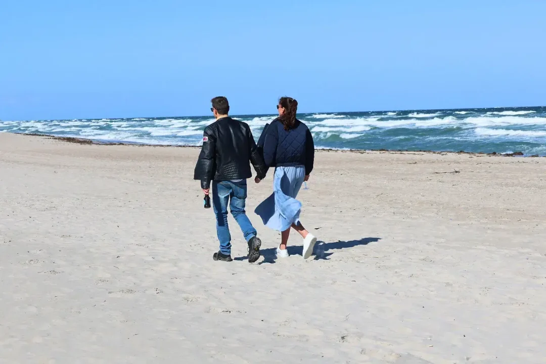 Ein Paar, das Hand in Hand am Strand des Ostsee-Resorts Damp spazieren geht.