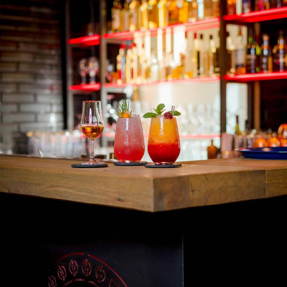Helle Cocktails und Rosé an der Bar, dahinter rot beleuchtete Regale.