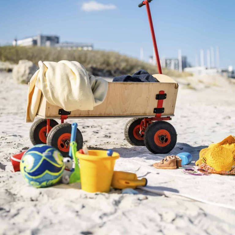 Holzwagen und Strandspielzeug im Sand in der Nähe des Familienhotels.