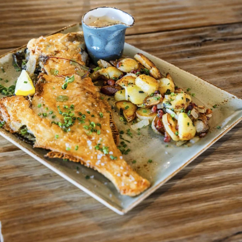 Ganzer gekochter Fisch mit Kartoffeln und Soße auf dem Holztisch.