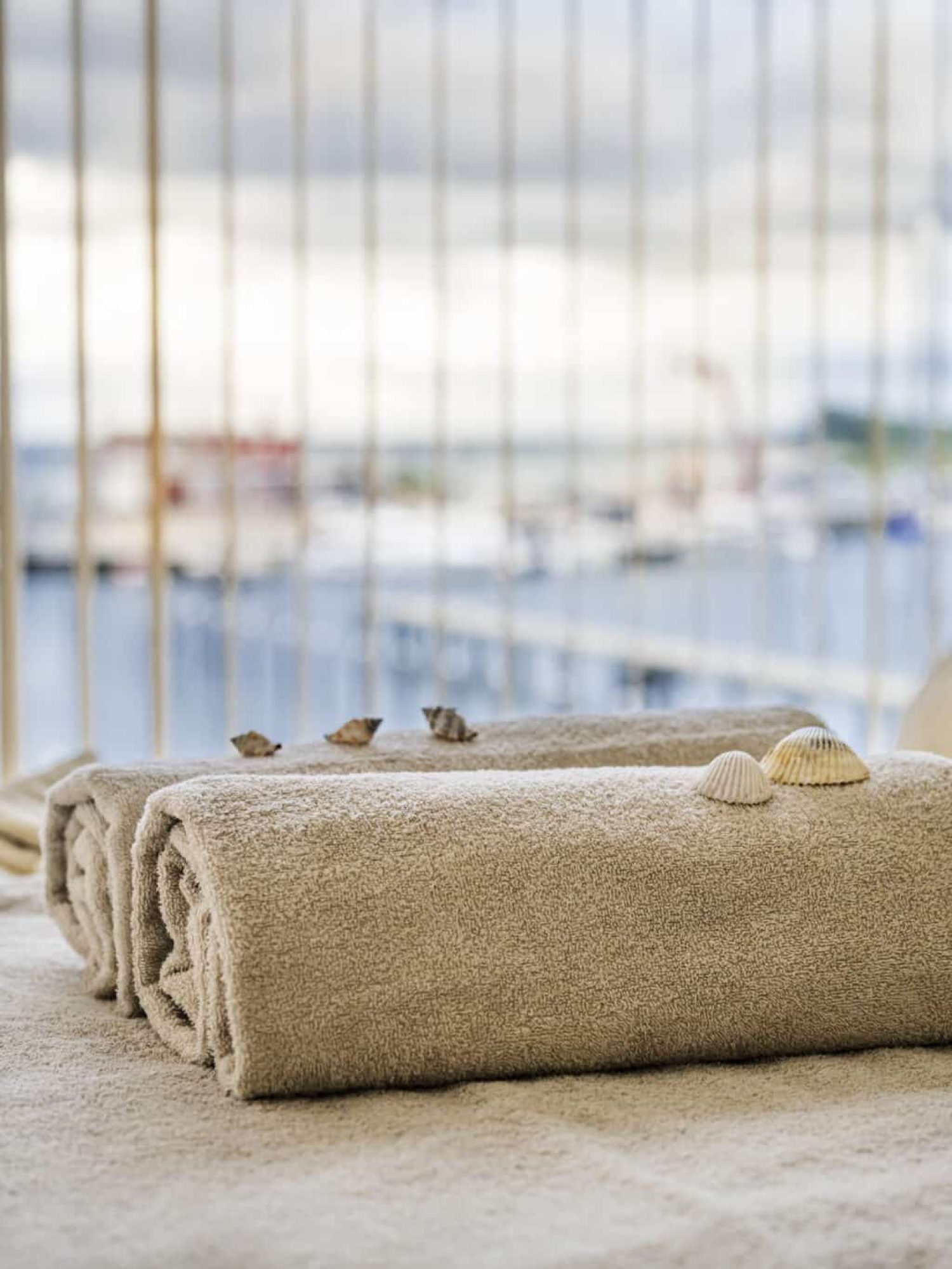 Beige Handtücher mit Muscheln auf dem Spa-Tisch, Blick auf den Yachthafen.