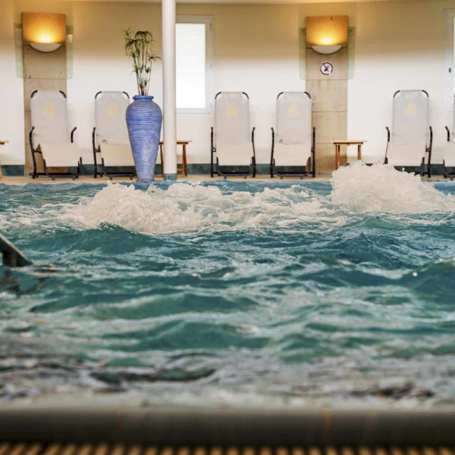 Innenpool mit blauem Wasser, Liegestühlen und Pflanzen.