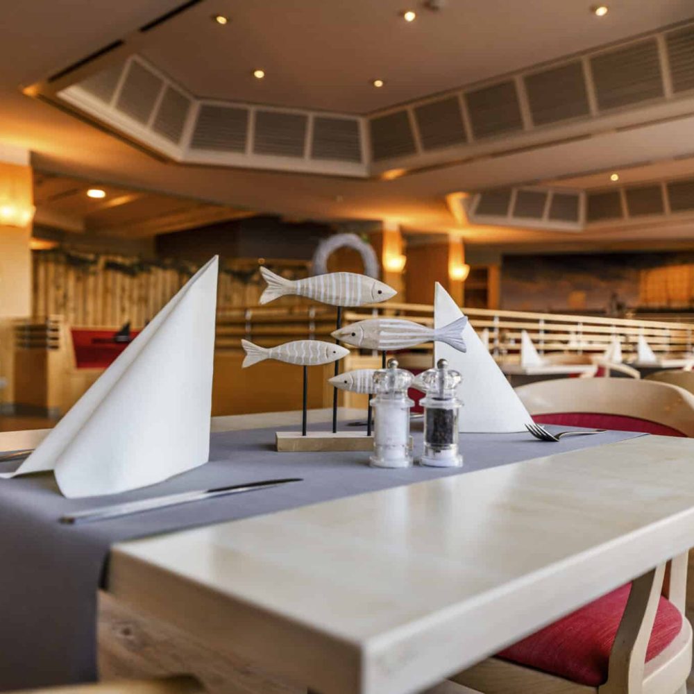 Gemütlicher Ostsee-Restauranttisch mit Servietten, Besteck und Fischdekor.