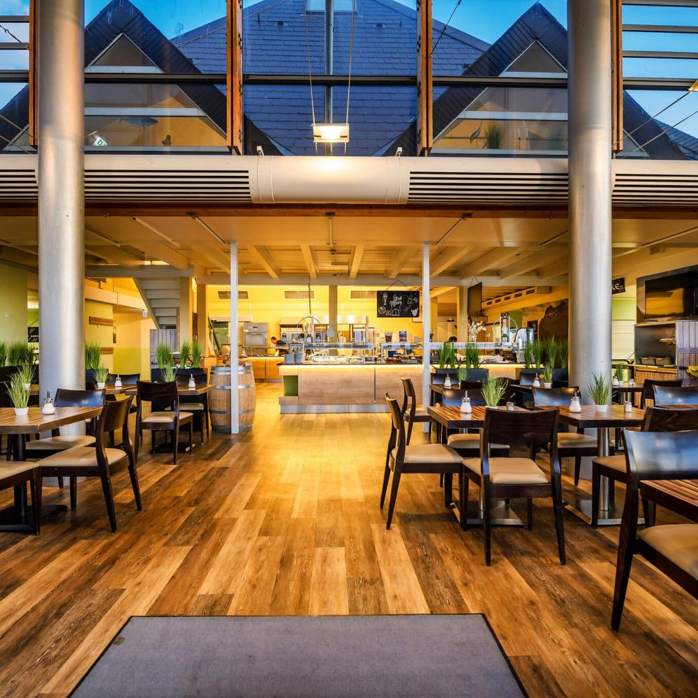 Modernes, geräumiges Restaurant mit Holzböden, Pflanzen, offener Küche.