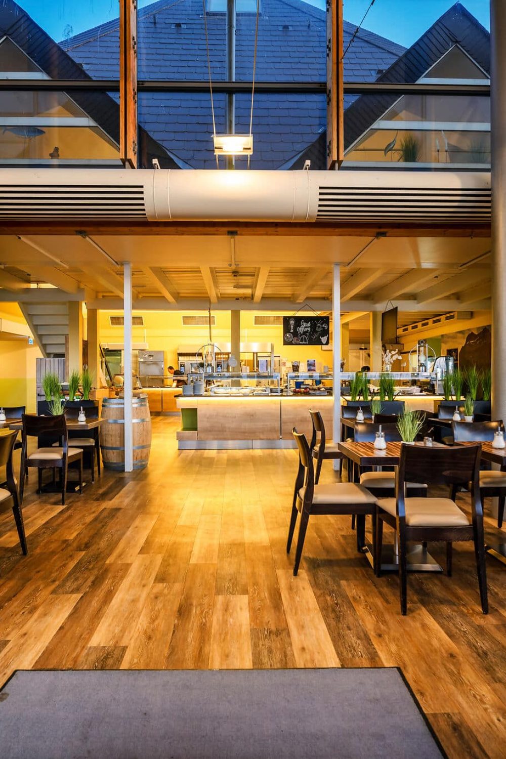 Modernes, geräumiges Restaurant mit Holzböden, Pflanzen, offener Küche.