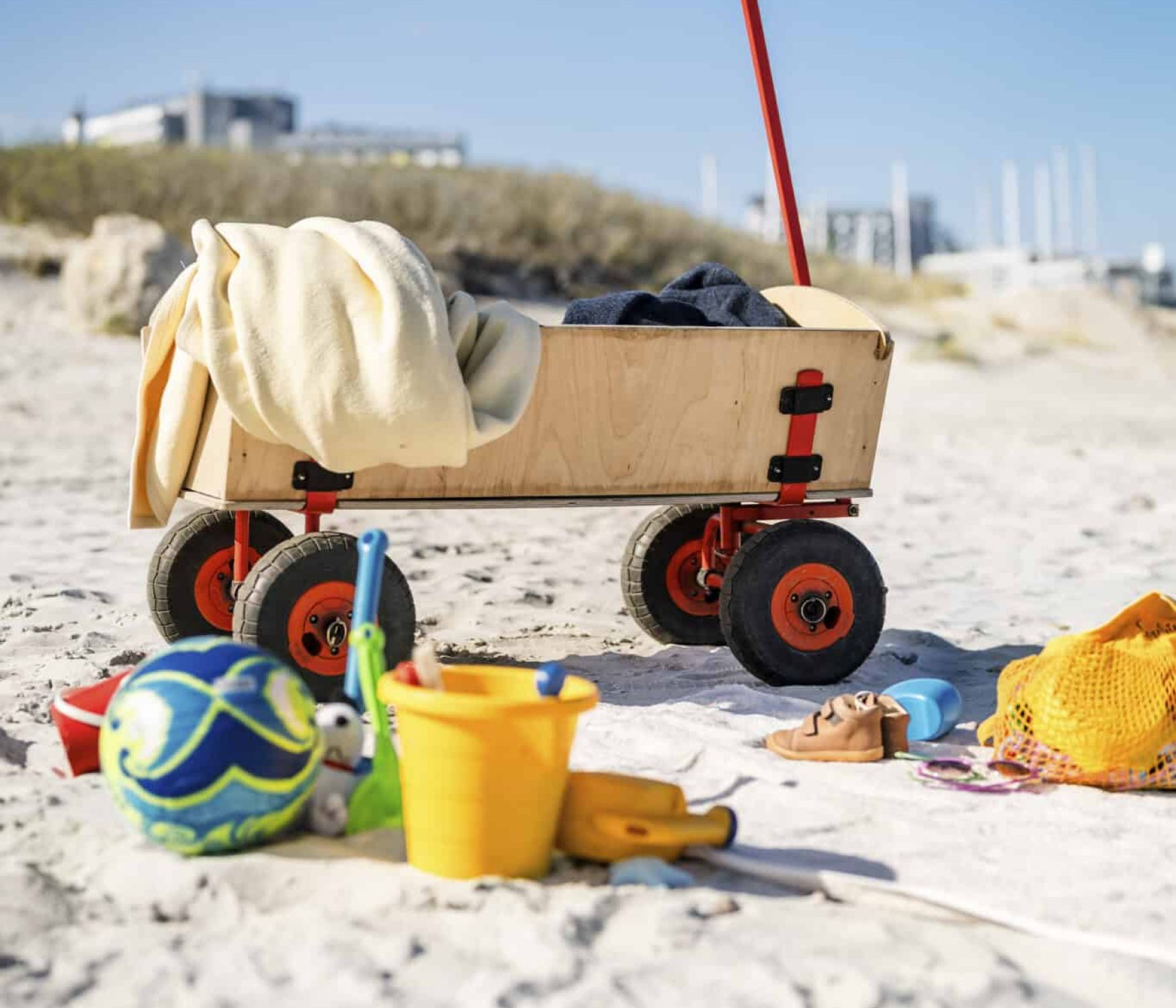 Wagen mit Kleidung, Spielzeug und Handtuch am Sandstrand.